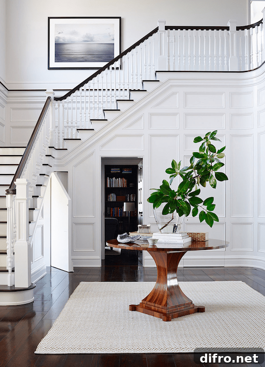 Stunning foyer features full wall wainscoting hiding door leading to secret room situated behind round entry table atop jute rug layered over glossy wide plank floors.