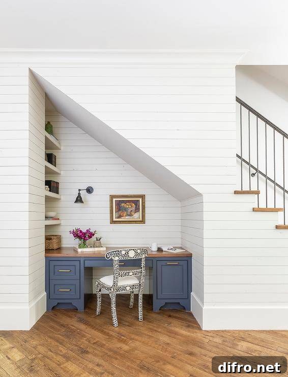 Beneath a staircase, a blue desk with a butcher block top sits on a diagonal wood floor and is built-in beneath an art piece hung from a wall covered in shiplap trim.
