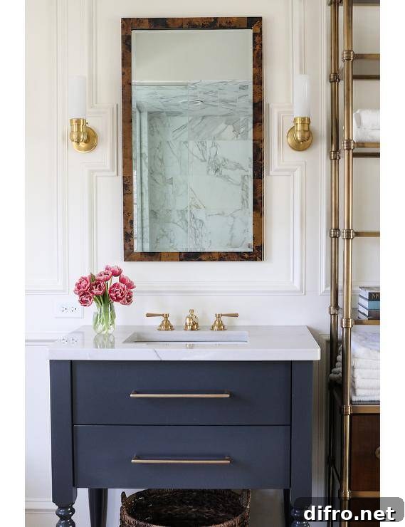 Transitional bathroom with a burl wood mirror flanked by brass sconces mounted on millwork walls above a black washstand topped with marble countertop and a brass vintage faucet. A brass etagere brings a French appeal to the bathroom displaying decor and bathroom essentials.