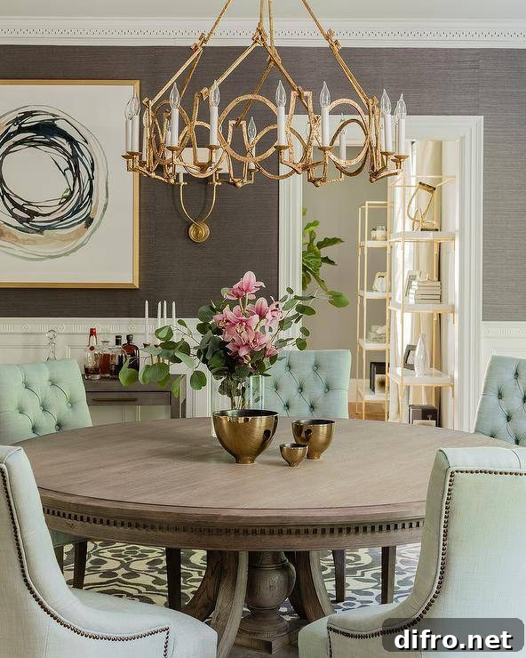 A gold leaf ring chandelier takes center stage over a round wood dining table surrounding green tufted linen chairs. Brass tableware, lovely floral centerpiece, and elegant background decor bring a transitional dining room design to life. Symmetric Twist Sconces next to a gold and black abstract wall art increases the room's ambience and attraction.