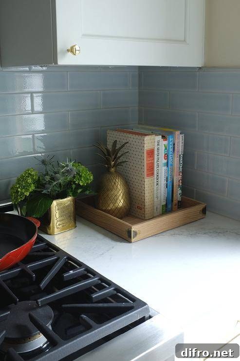 White and gray natural stone countertops in a small kitchen designed with white shaker cabinets and brass knobs. Sky blue subway tiles bring a charming color tone to space upgraded with stainless steel appliances and brass decor.