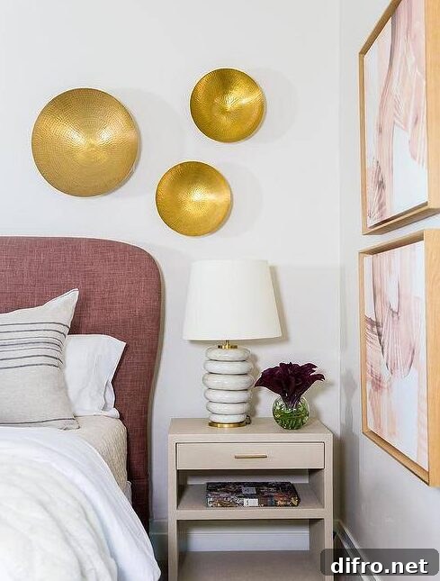 Chic bedroom updated with a mauve headboard and a light taupe nightstand displaying marble rings lamp under hammered brass wall decor. White and pink abstract wall art faces the bed with an artistic and flare complementing the rose tones in the mauve headboard.