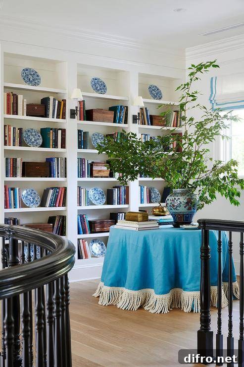 Staircase landing library features an azure blue fringe skirted table with potted plant and built in bookshelves.