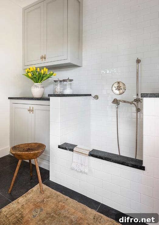 A tan vintage rug sits on slate floor tiles in front of a white subway tiled dog shower fitted with a polished nickel shower kit.