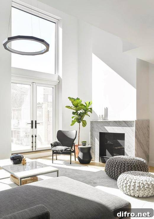 Chic modern living room boasts gray knitted stools placed on a gray rug in front of a modern gray marble fireplace, as a black accent table is paired with a black leather chair located in front of a fiddle leaf fig.