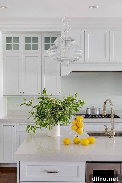 Kitchen with glass pendant lighting, off-white quartz counters and lush greenery accents.