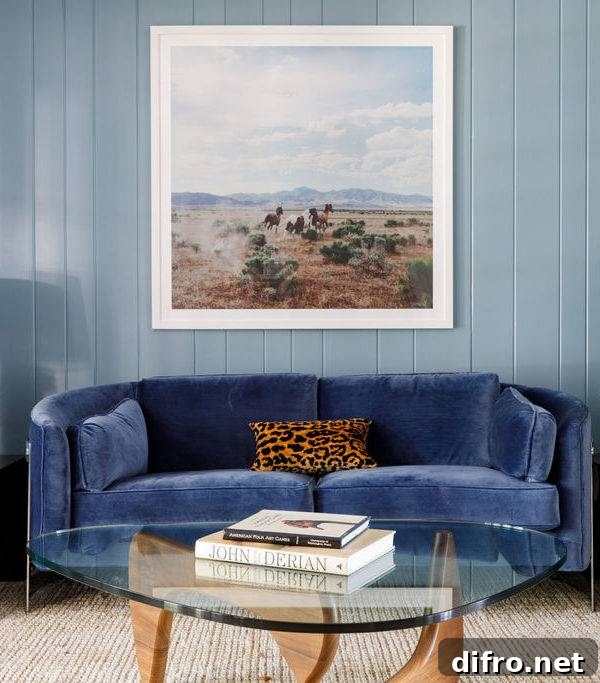 Living room features a curved blue velvet sofa with a leopard print pillow on a vertical blue plank wall with blue brown and white art, and a Noguchi coffee table