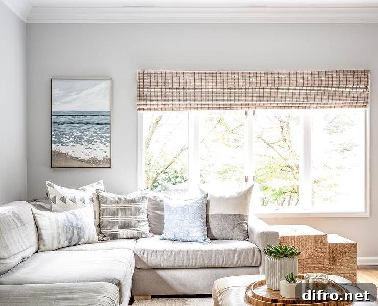 Light beige sectional in a living room paired with a light brown leather ottoman styled with stacked wood trays and a floral centerpiece. Various gray and white accent pillow style the sectional with a contemporary add on while a set of woven nesting end tables deliver a warm Scandinavian like feel.