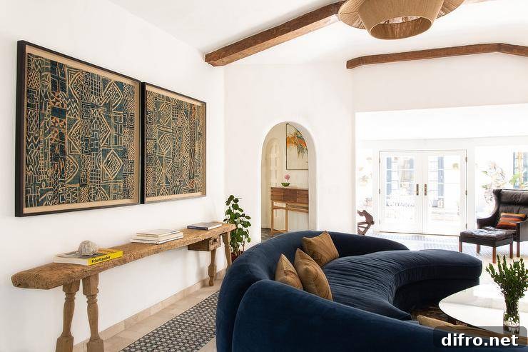 Vintage living room features reclaimed wood console table under framed fabric batik art and blue curved sofa with orange pillows.