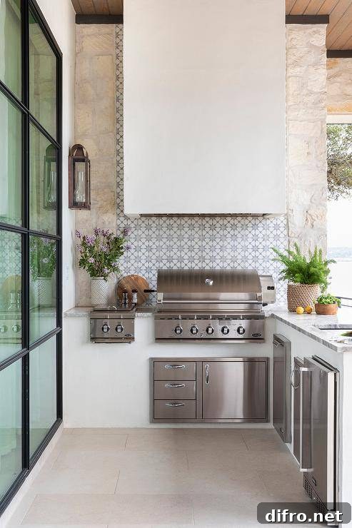 Well appointed l-shaped outdoor kitchen boasts a white hood fixed to gray and blue mosaic concrete backsplash tiles over a stainless steel BBQ.