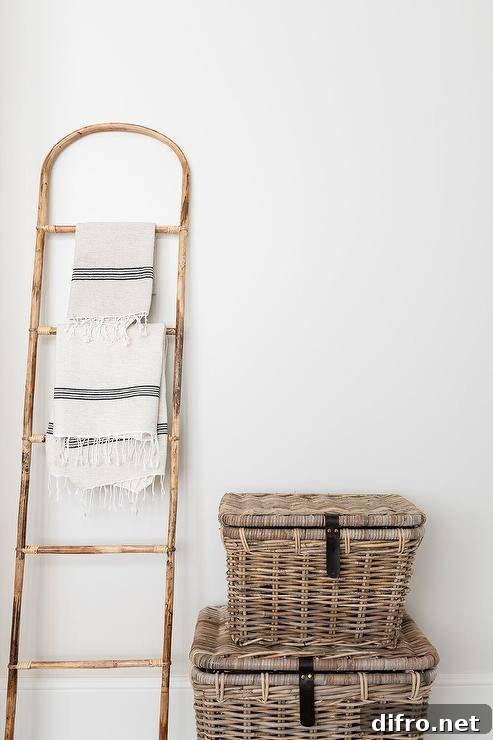 Cottage bathroom features a vintage towel ladder placed beside stacked wicker trucks.