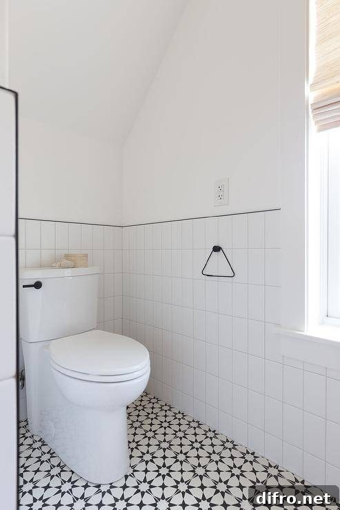 Half tiled vertical walls with black trim in a black and white bathroom boasting cement floor tiles under a vaulted ceiling.