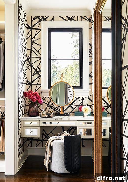 Makeup vanity nook with Kelly Wearstler Channels wallpaper features a gray fabric and black leather vanity stools at a mirrored makeup vanity under a window.