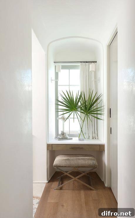 A cowhide bench sits in a makeup vanity nook at a brown floating vanity positioned under a window dressed in short white curtains.