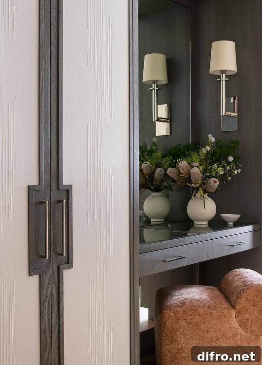 A pink velvet stool sits at a gray veneer makeup vanity lit by a nickel sconce next to a closet.