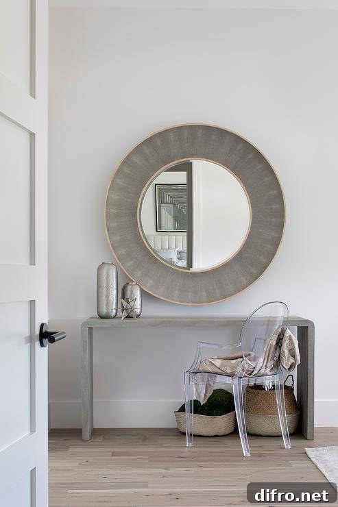 A ghost chair sits at a gray waterfall makeup vanity positioned beneath a round gold and gray shagreen mirror.
