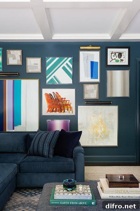 Living room features pictures lights over an art gallery on a peacock blue wall, a blue sectional and a blue ottoman as coffee table.