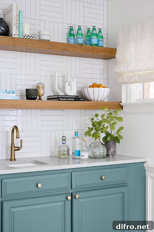 Blue kitchenette cabinetry boasts an antique brass gooseneck faucet fixed beneath stacked floating shelves mounted to white basketweave wall tiles.