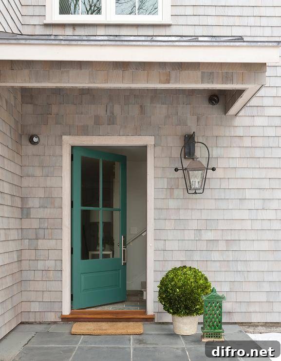 Gray cottage home features a green front door and a brown mat on slate pavers.