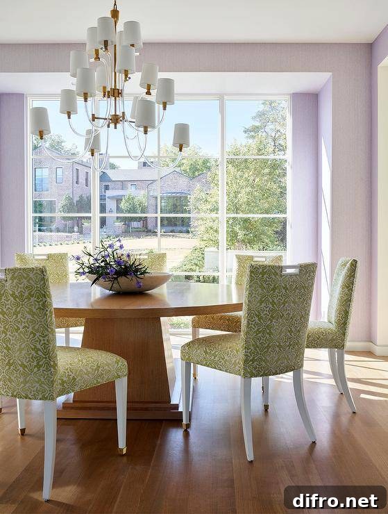 A glass and brass chandelier hangs over a round brown pedestal dining table paired with white and green damask dining chairs.