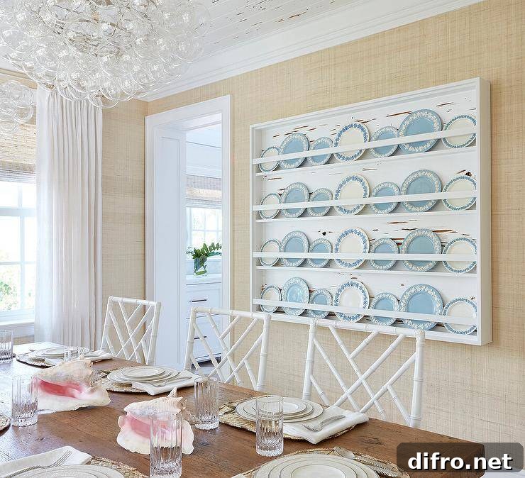 White bamboo lattice dining chairs sit at a reclaimed wood dining table lit by a glass bubbles chandelier and in front of a white plate display rack fixed to a wall covered in beige wallpaper.