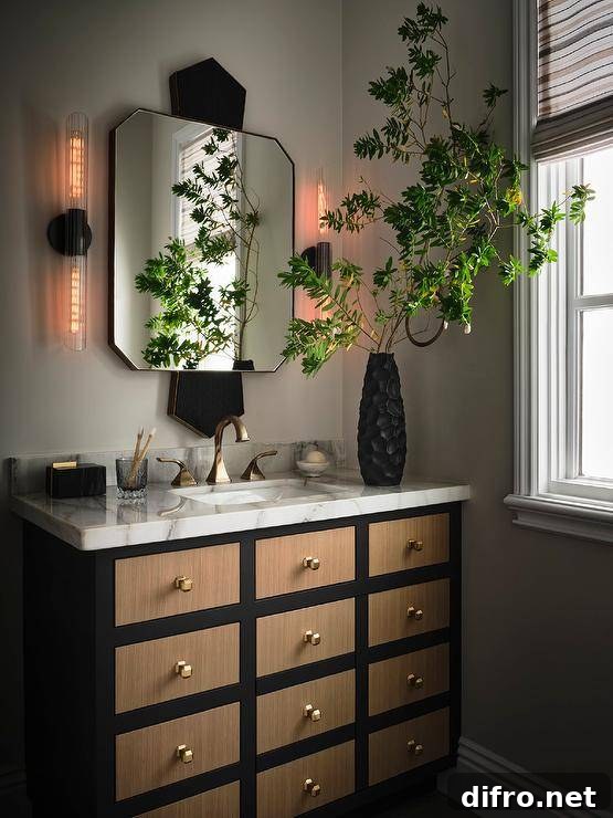 Bathroom features a brown and black apothecary style washstand with brass knobs and a marble countertop with brass faucet under a gold and black mirror flanked by long sconces.