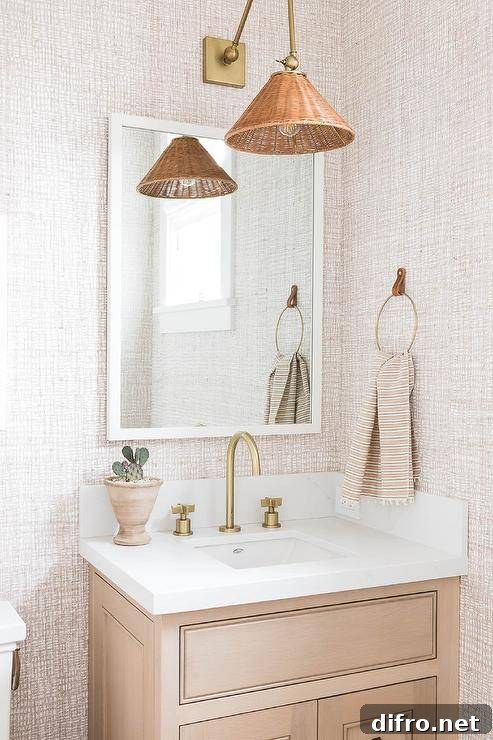 A tan washstand fitted with a gold gooseneck faucet is positioned beneath a white framed vanity mirror hung from a wall clad in tan textured wallpaper beneath a Cerro Wall Sconce.