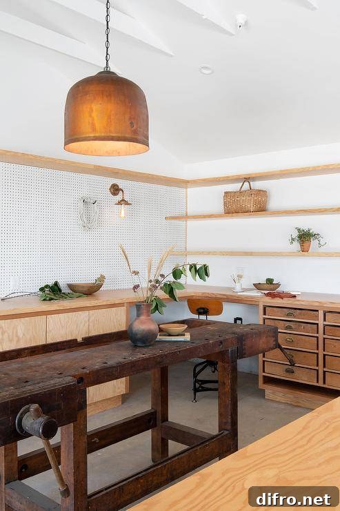 Cottage work space features a vintage work table, wooden shelves, white peg boards and vintage wooden drawers.