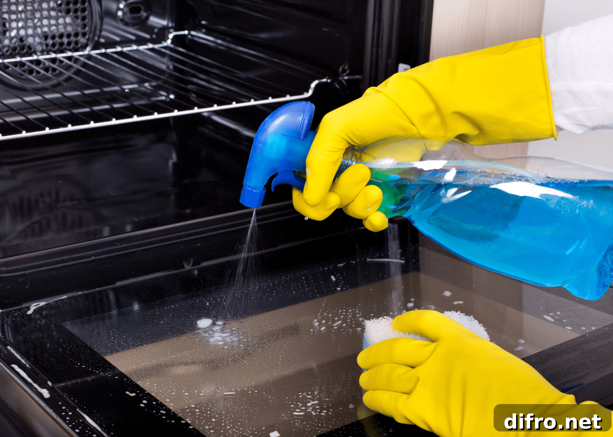 spraying an oven with a blue spray bottle