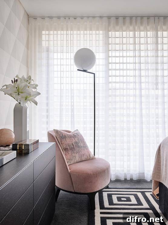 Modern bedroom features a pink velvet chair on a black and white geometric rug, a black dresser and white curtains, lit by a black and white floor lamp.