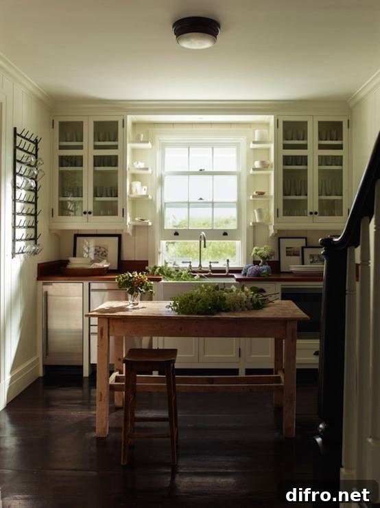 Lovely cottage kitchen with glass-front upper cabinets and white shaker lower cabinets paired with wood countertops and paneled backsplash. Oil-rubbed bronze flushmount over farmhouse kitchen island lined with rustic bar stool over wood floors. Kitchen features farmhouse sink under double hung window next to stainless steel stacked stacked dishwashers and mini-fridge.