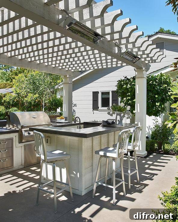 Gray pergola features an outdoor kitchen with navy counter stools at an island with a concrete countertop.