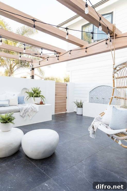 Backyard oasis features a custom water fountain and string lights lighting a pergola fitted with an extra large rattan hanging chair.