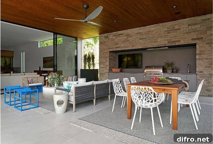 Covered patio features white laser cut outdoor dining chairs at a teak outdoor dining table atop a gray lattice outdoor rug.