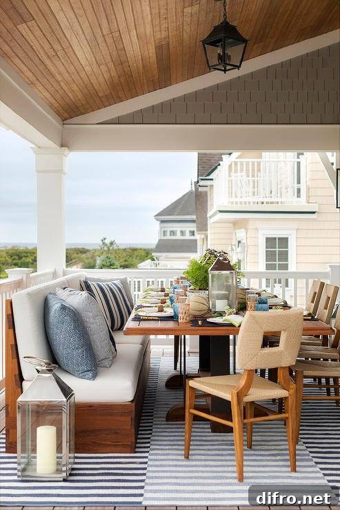 Abaca dining chairs sit on a covered deck on a black and white striped rug placed beneath a teak slatted dining table.