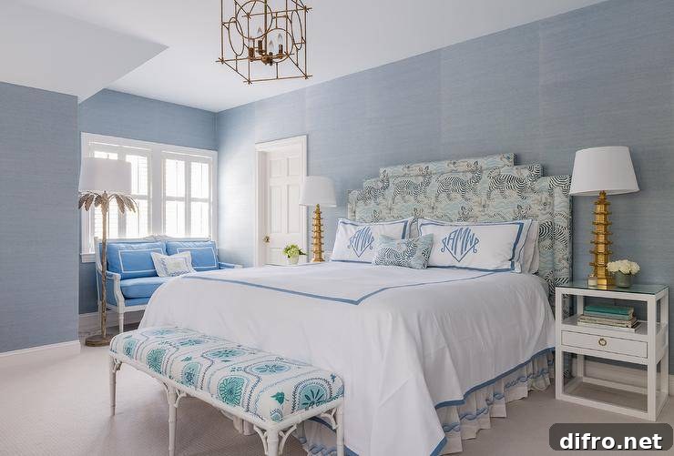 Positioned against a wall clad in blue grasscloth wallpaper, a headboard in Clarence House Tibet fabric supports a bed dressed in white and blue bedding topped blue monogrammed shams.