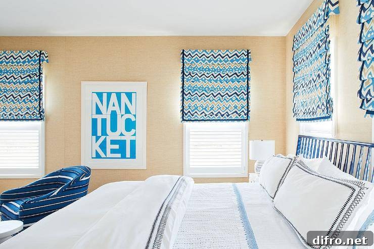 Tan wallpaper covers the walls of a white, blue, and tan bedroom featuring windows covered in tan and blue geometric roman shades flanking white and blue typography art.