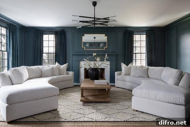 A raffia coffee table sits on a lattice rug between curved white sofas under a black and silver chandelier.