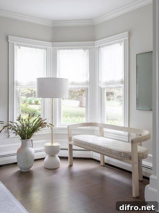 A light taupe curved bench and a white-and-taupe cushion under a white and brass floor lamp with a tall potted plant.