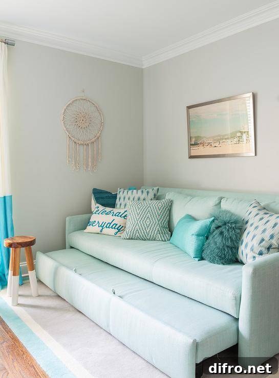 Serena & Lily Dip Dyed Stool beside an aqua blue sofa trundle bed decorated with various blue accent pillows against a gray wall in a girl's bedroom.