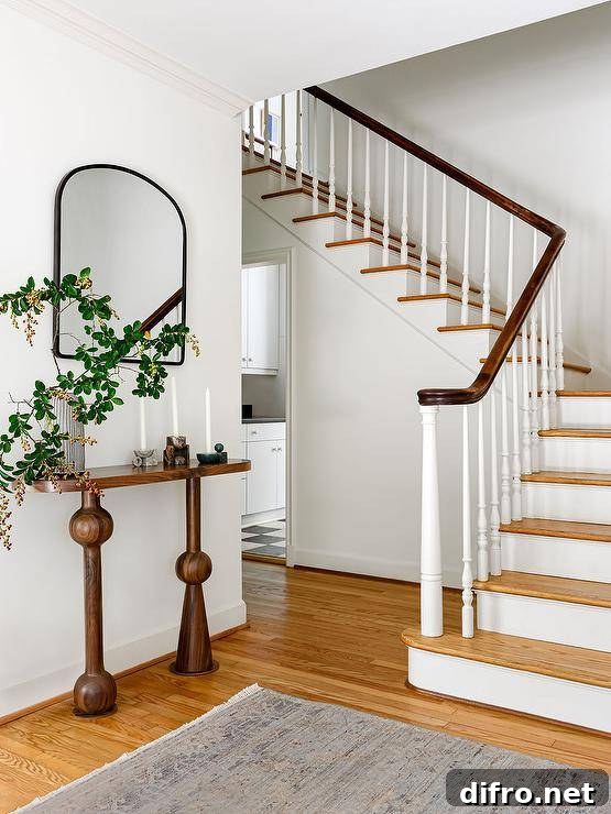 A black arch mirror hangs in a foyer over a brown oval console table.