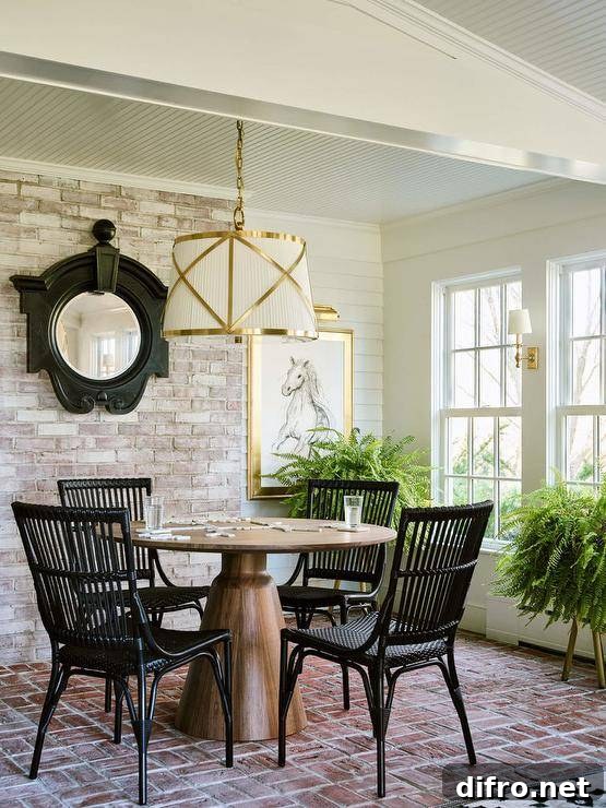Cottage sunroom with wicker chairs and a pedestal game table, illuminated by a brass and white pendant.