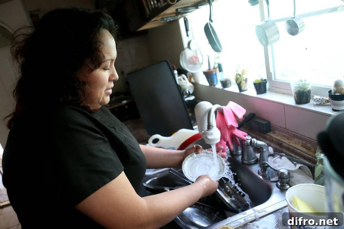 A woman washes dishes by hand in her kitchen.