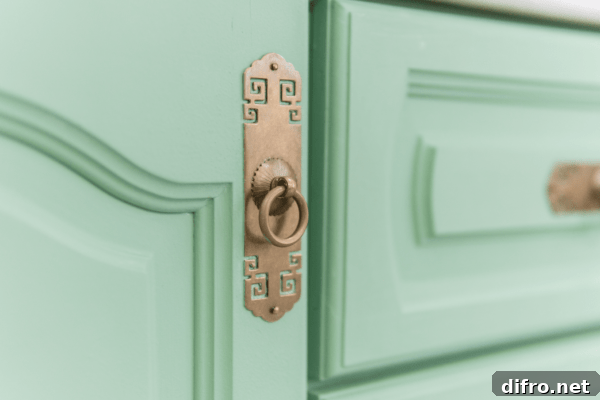 A closeup of a fancy gold drawer pull on a mint green cabinet door.
