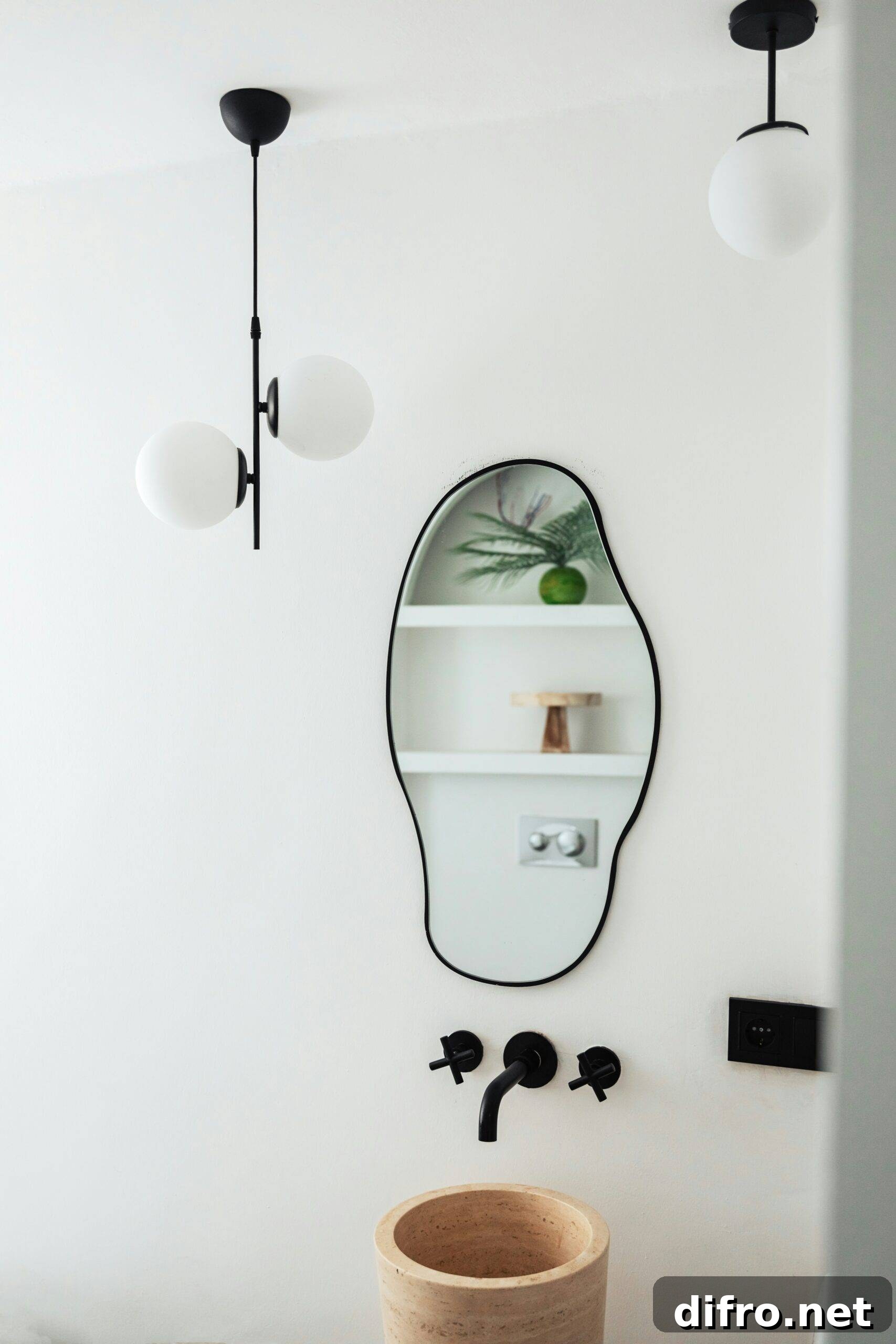 An uneven oval shaped mirror above a small, modern sink in a bathroom.