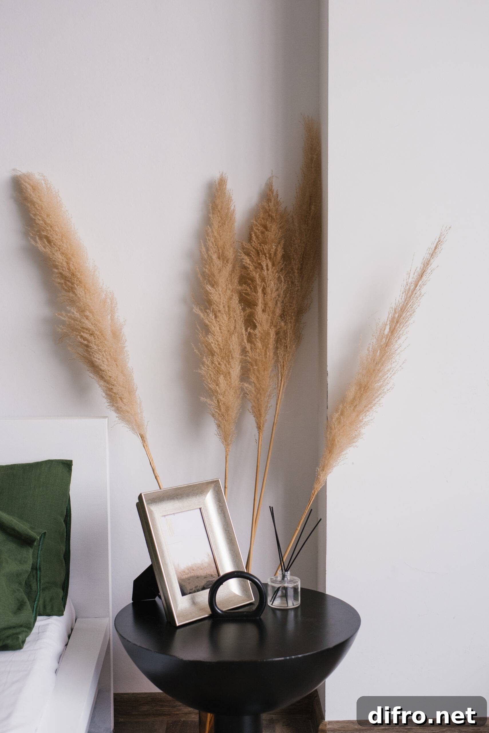 Tall pampas grass stalks behind a night table, a bed beside it.
