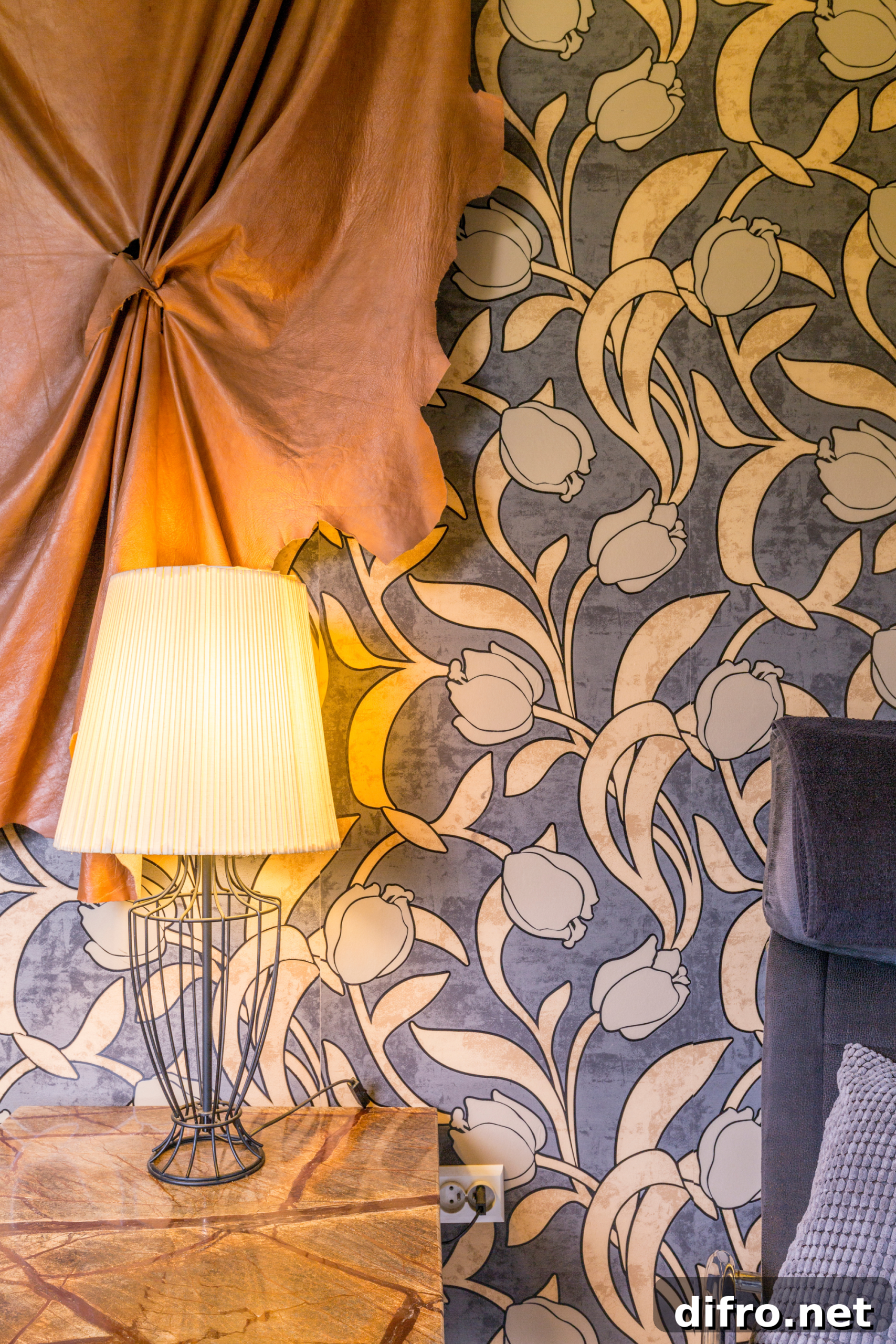 A beside table and a turned-on lamp, a curtain, and wallpaper on the wall.