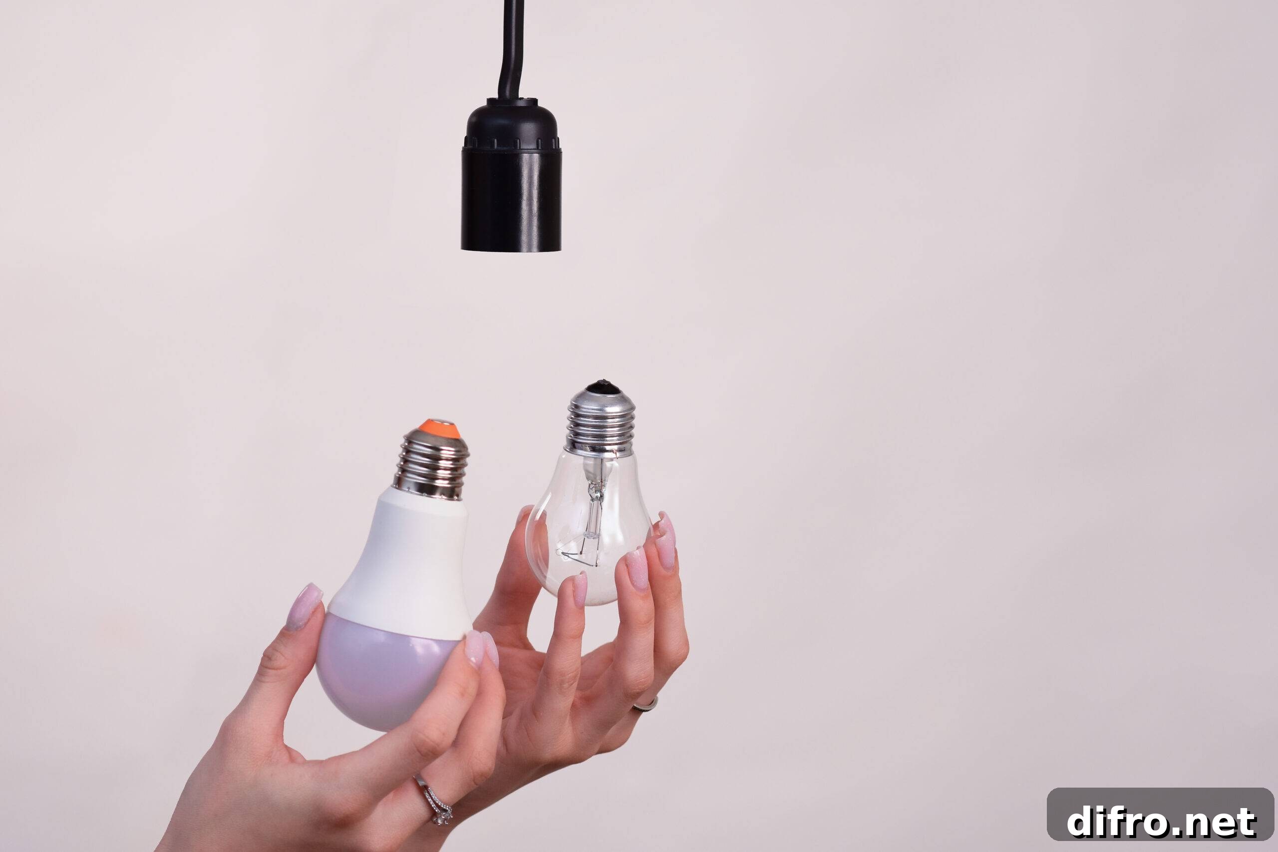 Two hands holding an incandescent lightbulb and an LED lightbulb.