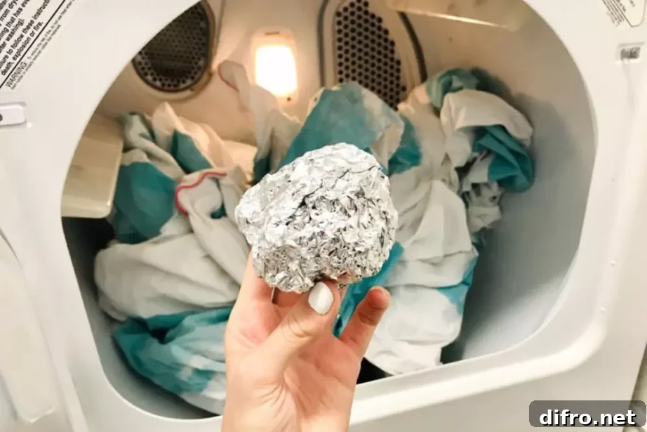 A hand holding up a balled up piece of tinfoil in front of an open dryer.