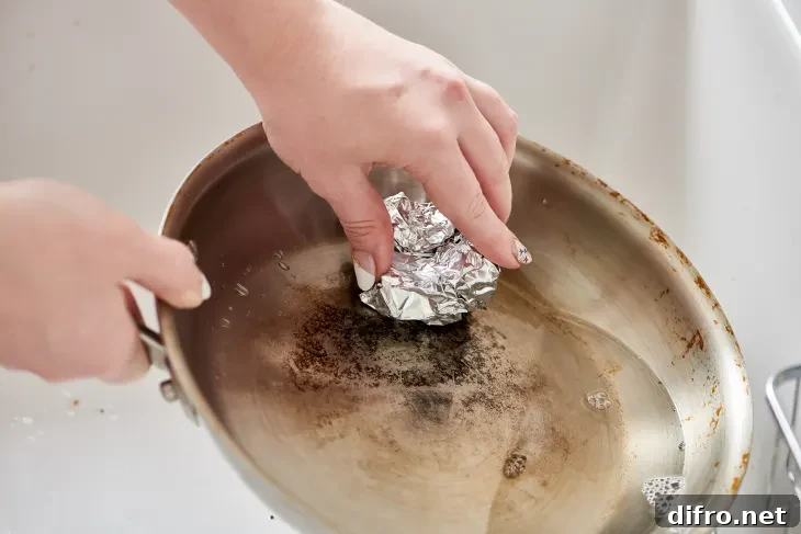 Someone using a balled up piece of tin foil to scrub at a pan.